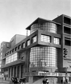 an old black and white photo of people walking in front of a building with many windows