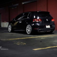 the back end of a black car parked in a parking lot next to a building