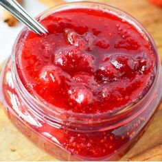 a jar filled with raspberry jam sitting on top of a wooden cutting board