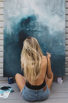 a woman sitting on the ground in front of a large painting with her back to the camera