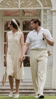 a man and woman walking on the grass holding tennis racquets