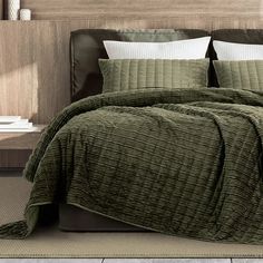 a bed with green bedspread and pillows in a room next to a wall