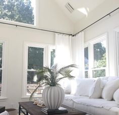 a living room filled with white furniture and lots of windows on the side of it