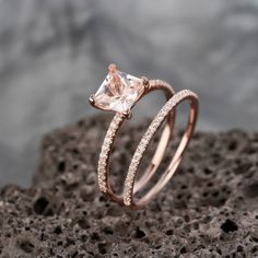 two wedding rings with an morganite and diamond set on top of each other in front of a rock