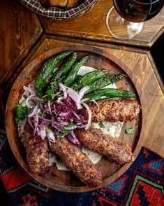 a wooden plate topped with meat and veggies next to a glass of wine