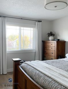 a bedroom with a bed, dresser and window covered in white drapes on the windowsill