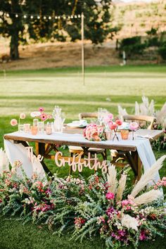 a wooden table with flowers and greenery on it in the middle of a field