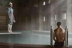 a man sitting on the edge of a swimming pool next to a woman in a bathing suit