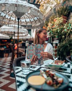 a woman sitting at a table with an open book in front of her and eating food