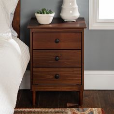 a nightstand with two drawers and a potted plant on it next to a bed