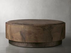 a round wooden table sitting on top of a cement floor next to a white wall