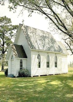 a small white church sitting on top of a lush green field next to tall trees