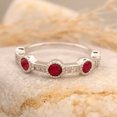 a white gold ring with three red stones on the side and two diamonds in the middle