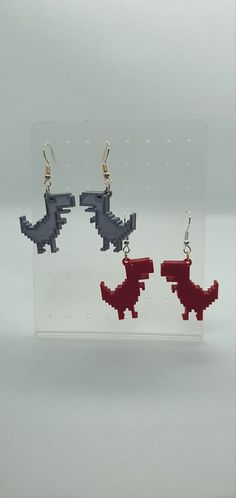 two red and black dinosaur shaped earrings are shown in front of a clear acrylic display