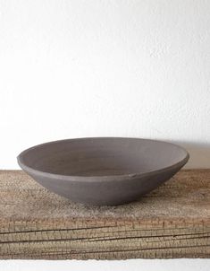 a gray bowl sitting on top of a stack of wooden boards next to a white wall