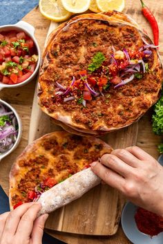 two pizzas sitting on top of a wooden cutting board next to bowls of vegetables