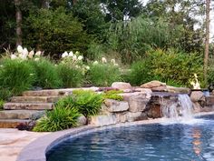 an outdoor pool with waterfall and rock steps leading up to the water feature, surrounded by lush greenery