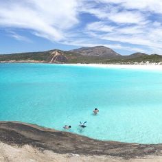 two people are swimming in the clear blue water near an island with white sand and mountains