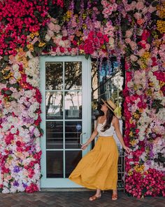 a woman standing in front of a door with flowers all over the wall and wearing a hat