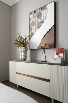 a vase with flowers on top of a white cabinet next to a painting and a bed