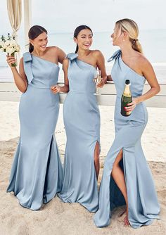 three beautiful women standing next to each other on top of a sandy beach with drinks in hand