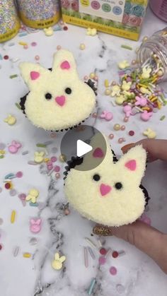 someone is holding two small cupcakes with bunny ears on them in front of confetti and sprinkles