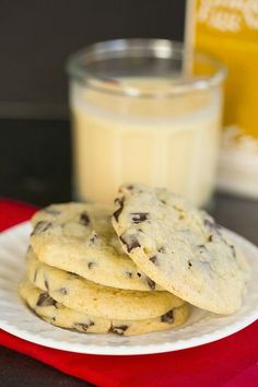 chocolate chip cookies on a white plate next to a glass of milk and a red napkin