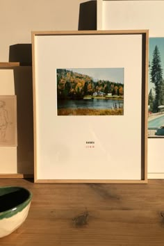 some pictures are sitting on a wooden table next to a bowl and vase with water in it