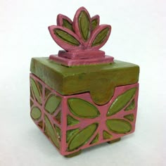 a green and pink box with a plant on it's top sitting on a white surface