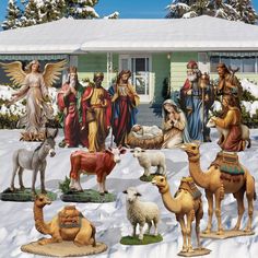 a group of christmas figurines in front of a house with snow on the ground