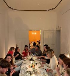 a group of people sitting around a dinner table with plates and wine glasses on it