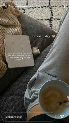 a person holding a cup of coffee next to a book on a couch with a blanket