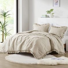 a bed with white sheets and pillows in a room next to a plant on the floor