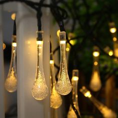 some light bulbs are hanging from the side of a fence with lights on them and trees in the background