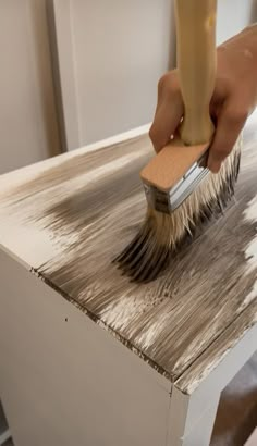 a person with a brush on top of a wooden table that has been painted white