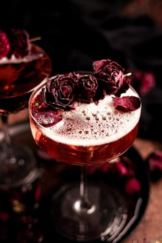 two glasses filled with liquid and flowers on top of a table next to each other