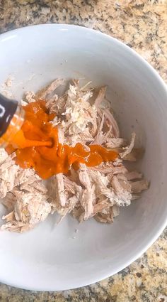 an orange sauce being poured into a white bowl filled with shredded meat and carrots