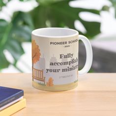 a coffee mug sitting on top of a wooden table next to a book and plant