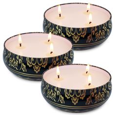 three lit candles sitting on top of each other in black and gold dishes with designs