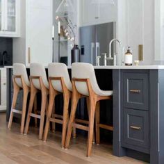 a kitchen with white cabinets and gray countertops, four chairs are lined up in front of the island