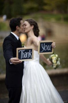 a bride and groom kissing while holding signs that say thank