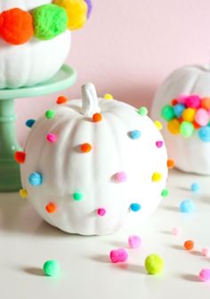 two white pumpkins decorated with colorful pom - poms on a cake stand