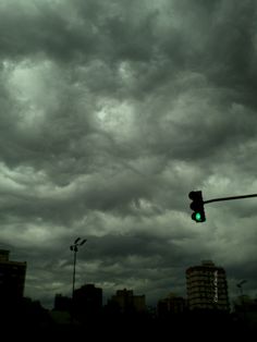 a green traffic light in front of some buildings under a cloudy sky with dark clouds