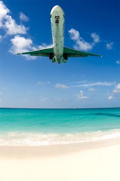 an airplane flying over the ocean on a sunny day with blue skies and white clouds