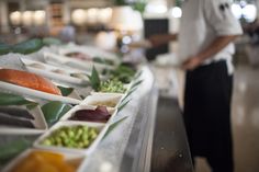 there are many different types of food on the buffet table, and one person is standing in the background