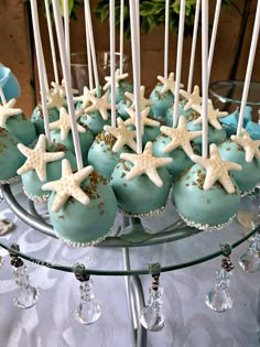 blue cake pops with white and gold stars on them sitting on a glass plate next to candles