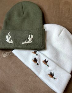 two beanies sitting on top of a bed next to each other with deer embroidered on them