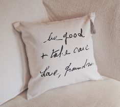 a pillow with writing on it sitting on top of a white couch next to pillows