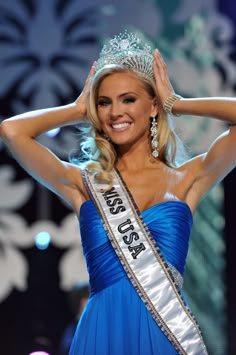 a beautiful woman in a blue dress and tiara posing for the camera with her hands on her head