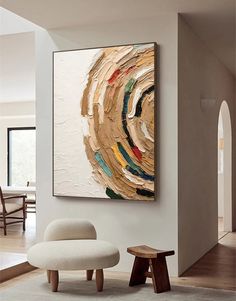 an abstract painting hangs on the wall next to a white chair and footstool